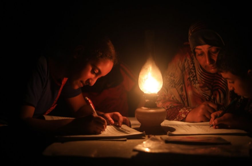 A woman helps children study under candle light during a power cut in Khan Yunis, Gaza on August 18, 2020. After Israel tightened the blockade in Gaza Strip, the only power plant in the area stopped production affecting the life especially the health sector. Photo by Mustafa Hassona. Anadolu Agency.